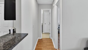 Ein Flur mit einer Granit-Arbeitsplatte, weißen Wänden, Holzboden und einer weißen Tür am Ende.