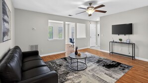Ein Wohnzimmer mit einer schwarzen Ledersofa, einem runden Couchtisch mit Dekorationselementen, einem Deckenventilator und einem flachbildfernseher an der Wand.