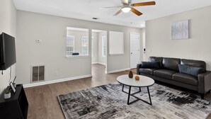 A living room with a ceiling fan, a black leather sofa, a round coffee table, and a gray rug.