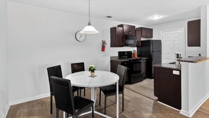 A modern kitchen with dark cabinets, a white dining table, and black chairs.