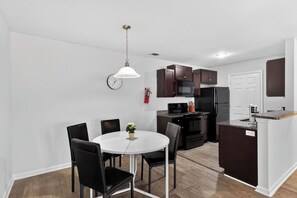 A modern kitchen with dark cabinets, a white dining table, and black chairs. - Modern 2BR/2BA Spacious Retreat (Savannah)