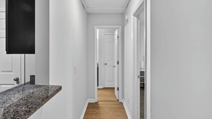 A narrow hallway with white walls, a wooden floor, and a granite countertop on the left.