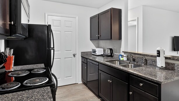 A kitchen with a stove, microwave, sink, and dark cabinets.
