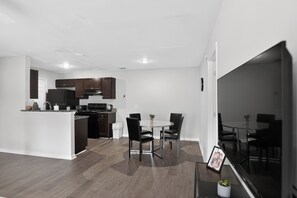 A modern kitchen with dark cabinets, a white island, and a dining area with a round table and chairs.