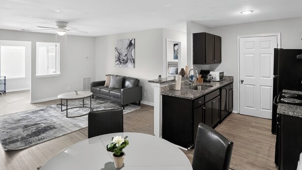 Et moderne køkken med mørke skabe, en central ø og et spiseområde med bord og stole.