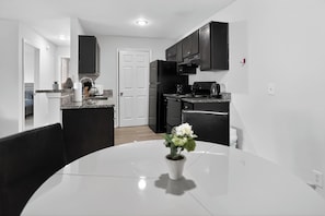 A modern kitchen with dark cabinets, a white countertop, and a dining area with a white table and chairs.