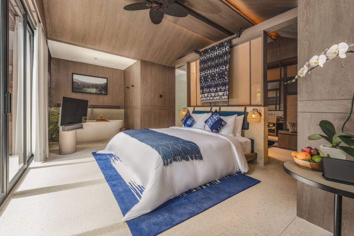 A modern bedroom with a bed, a desk, a television, and a view of the outdoors.