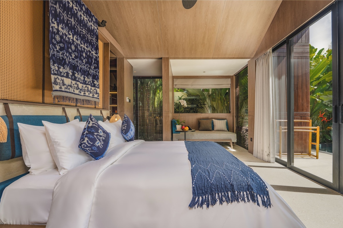 Un dormitorio moderno con una cama grande, un sofá y vistas a zonas verdes a través de la puerta de cristal.