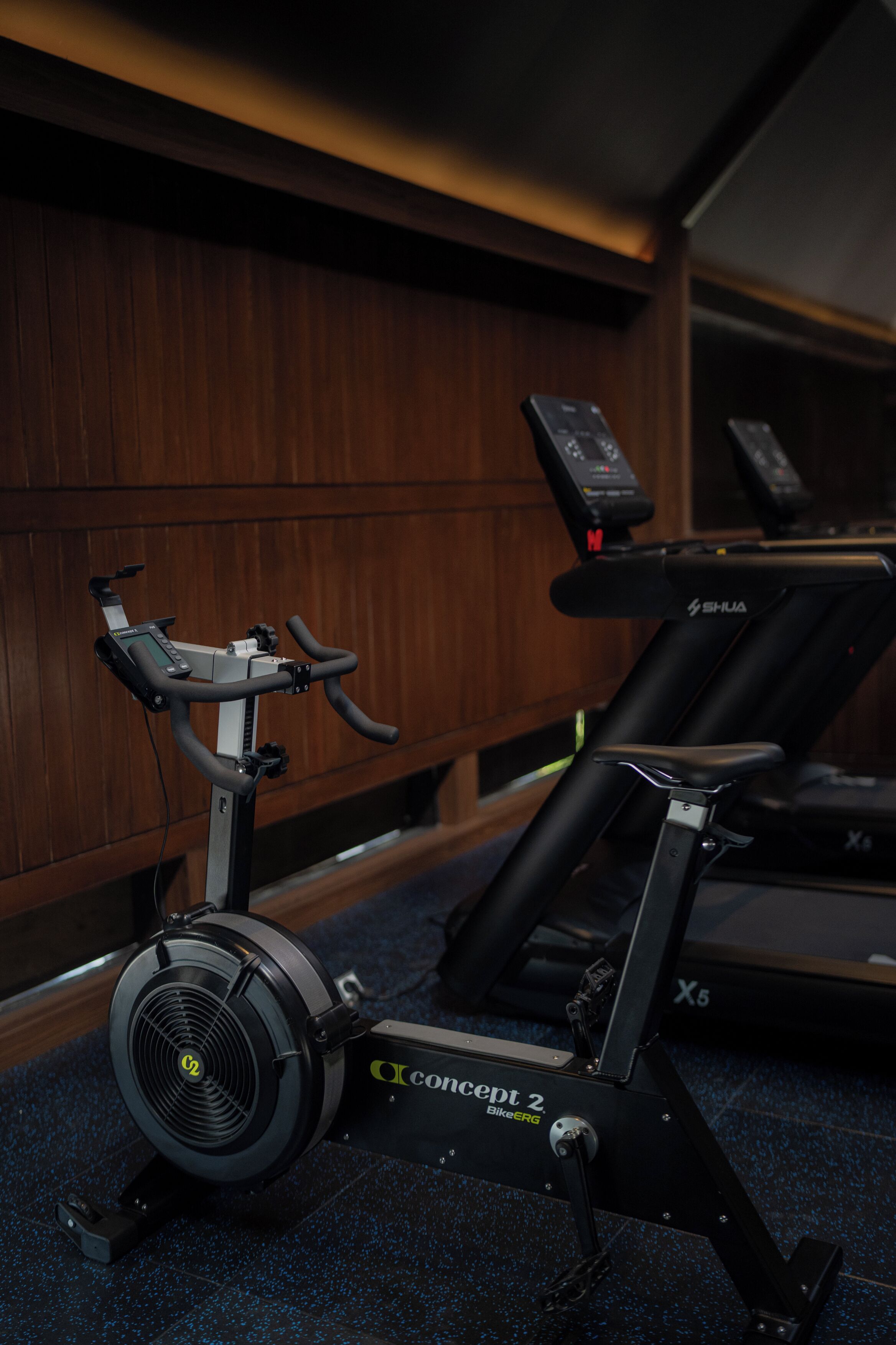 Una bicicleta estática con pantalla digital y una cinta de correr al fondo.