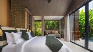 Un dormitorio con una cama grande, un sofá, una mesita y vistas a zonas verdes a través de amplias ventanas.