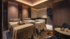 Un cuarto de spa con varias camillas de masaje, una mesa redonda con sillas y una pared de piedra.