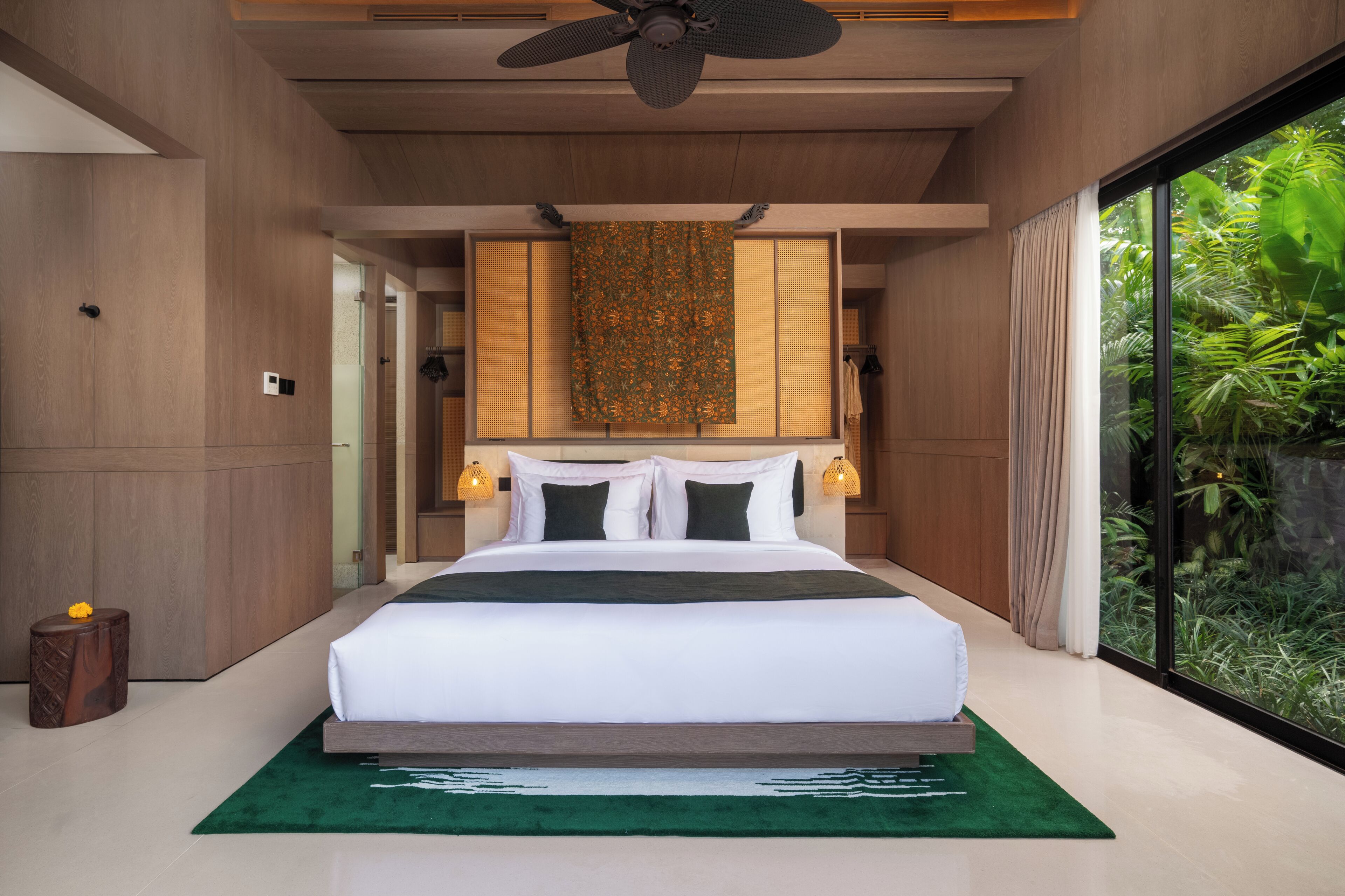 A modern bedroom with a large bed, a ceiling fan, and a view of greenery outside.