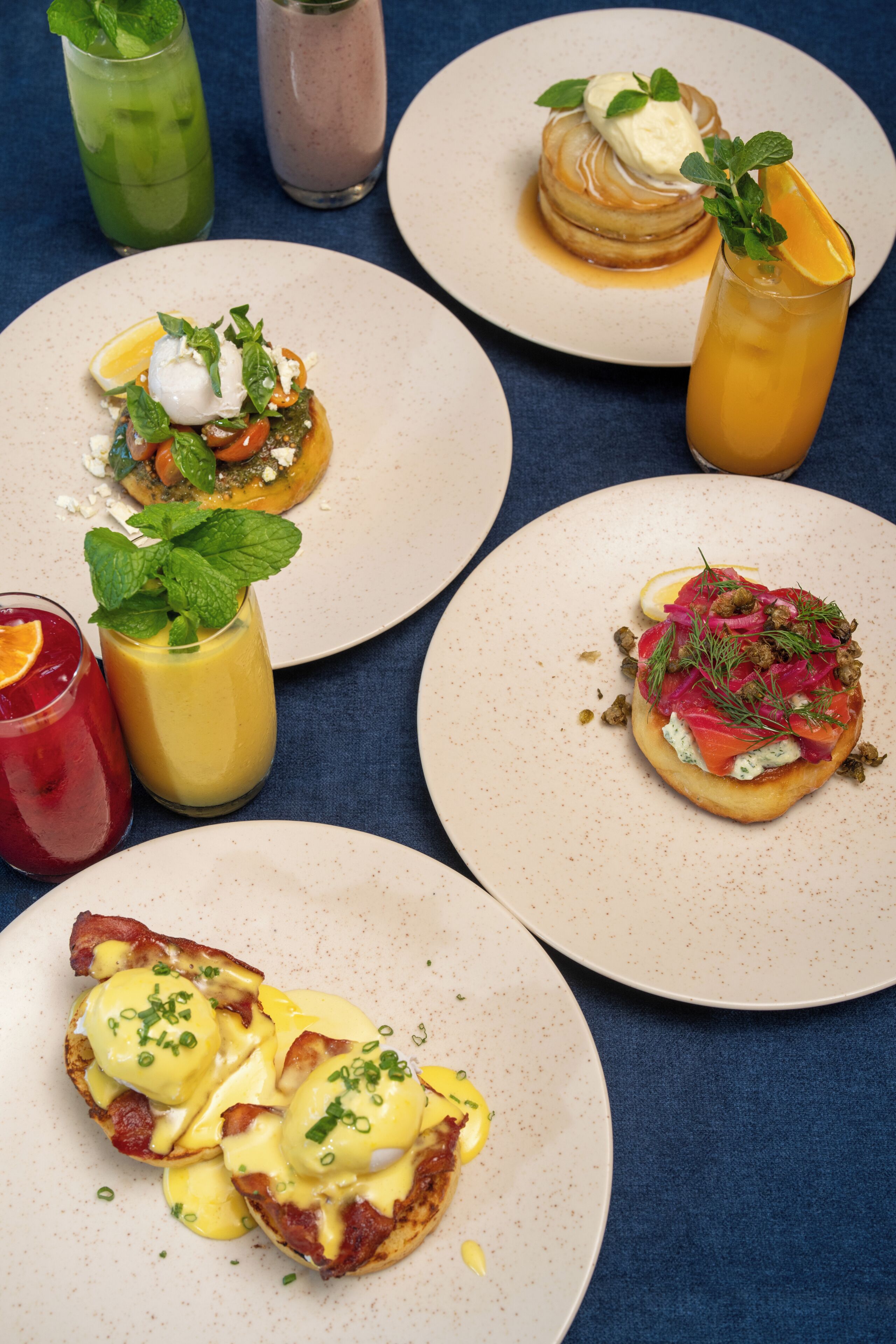 A variety of breakfast dishes on plates, including pancakes, eggs, and a smoothie.
