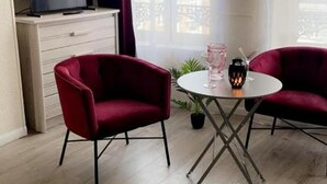 Moderni huone, jossa on televisio kaapissa, kaksi punaista tuolia pyöreän pöydän ympärillä ja ruukkukasvi.