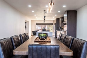 A modern dining area with a long wooden table surrounded by leather chairs, a central plant, and recessed lighting. - Beachfront Bliss Panoramic Ocean Views Sleeps 33 (Corpus Christi)