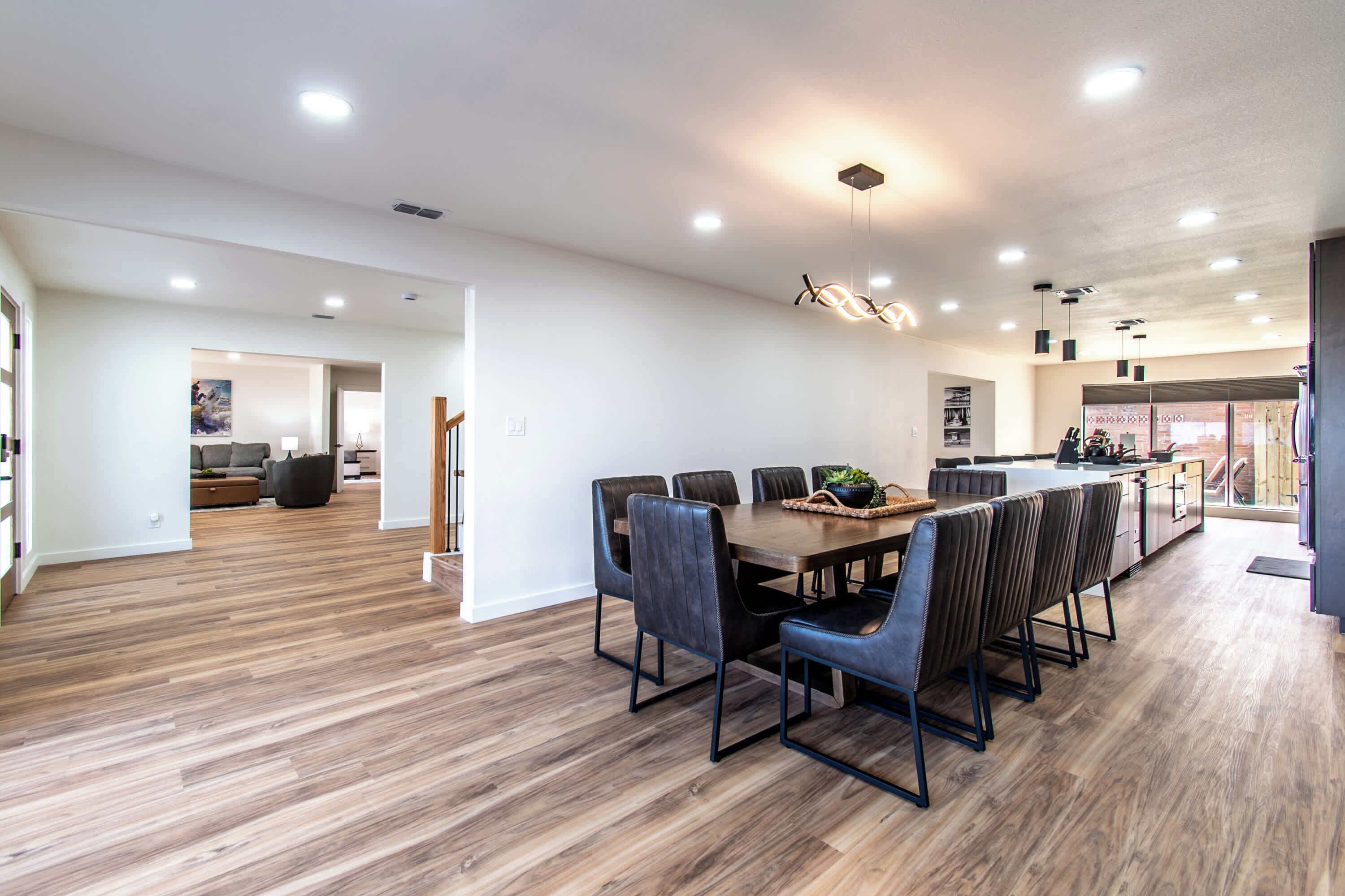 A spacious dining area with a wooden table and chairs, a kitchen in the background, and a modern ceiling design.