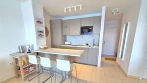 Una cocina moderna con una isla central, taburetes blancos de bar y una pequeña mesa de comedor.
