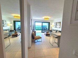 Ein modernes Wohnzimmer mit Sofa, Couchtisch und Sessel. Es gibt einen Essbereich mit Tisch und Stühlen. Das Zimmer verfügt über ein großes Fenster mit Meerblick.