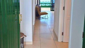Un pasillo que da a un balcón con vista al mar, una silla y un cubo de basura.