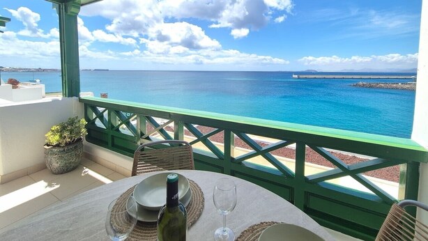 Una terraza con mesa lista para comer, con vista a un mar azul cristalino y una costa lejana.