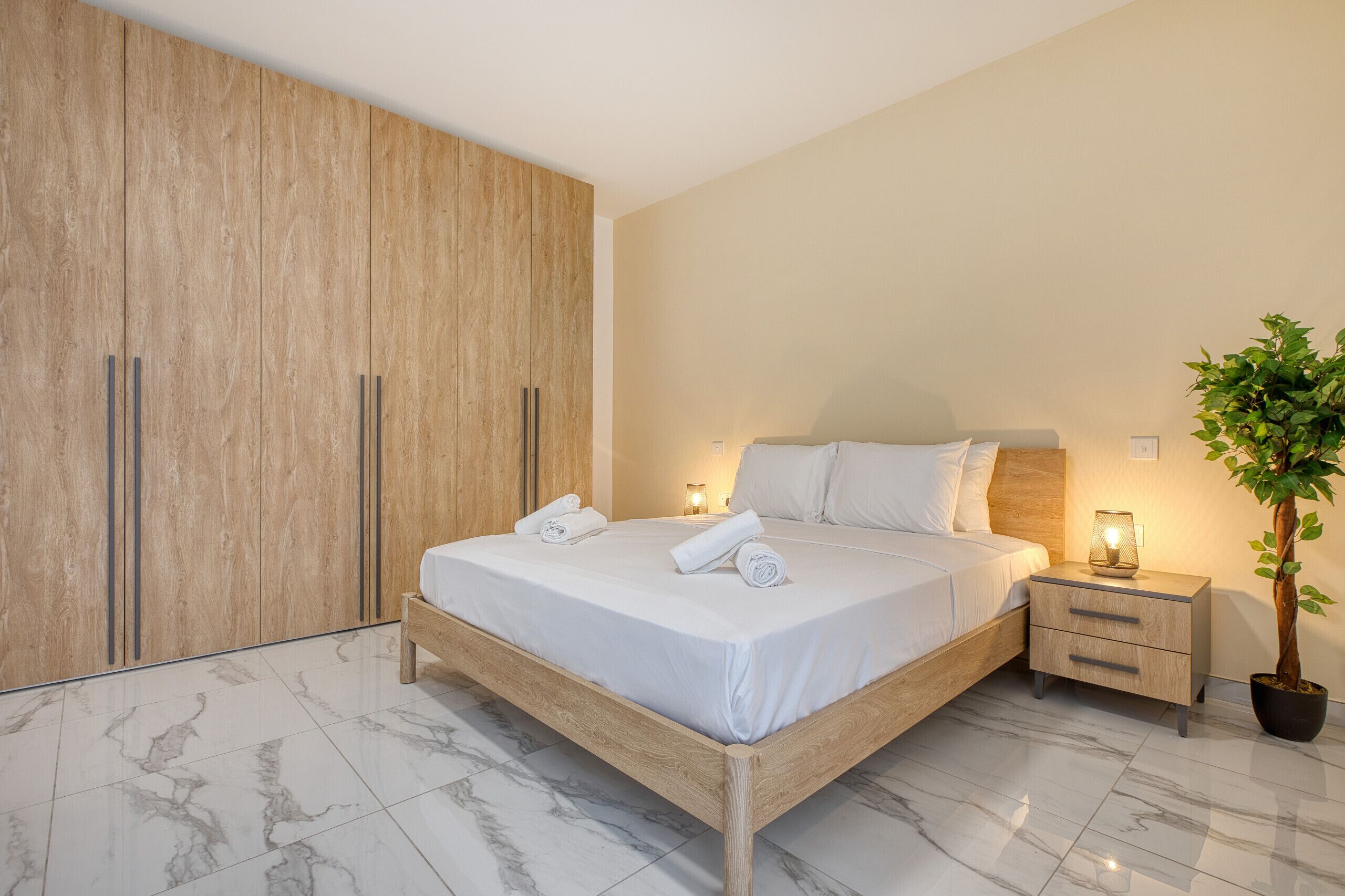Une chambre à coucher avec un lit en bois, une table de chevet, une plante en pot et une armoire.