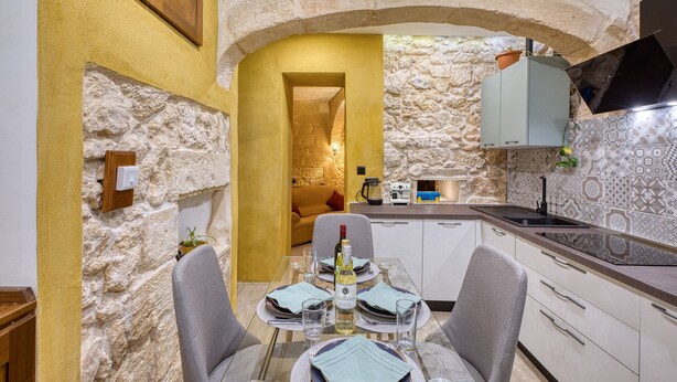 A dining area with a stone wall, a wooden cabinet, a table set for two, and a kitchen area with a sink and cabinets. - Beautiful traditional house in Rabat AMUS1-1 (Rabat)