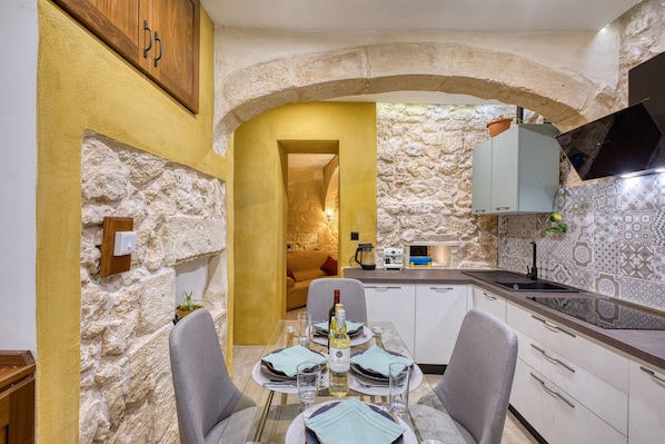A dining area with a stone wall, a wooden cabinet, a table set for two, and a kitchen area with a sink and cabinets. - Beautiful traditional house in Rabat AMUS1-1 (Rabat)