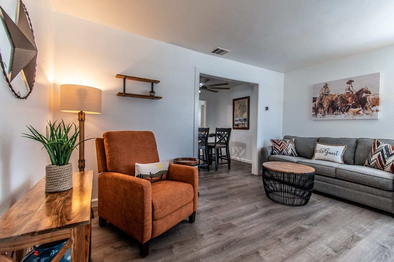 A living room with a sofa, armchair, round coffee table, and a dining area with chairs and a table.