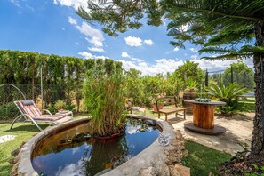 A backyard with a pond, lounge chairs, a wooden table, and various plants. - Finca with pool Can Pintat in Mallorca (Llubi)