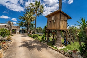 A wooden structure with a staircase, surrounded by palm trees and a pathway leading to a building. - Finca with pool Can Pintat in Mallorca (Llubi)
