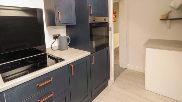 A modern kitchen with dark cabinets, a built-in oven, and a kettle on the countertop. - The Loft Apartment @ The Stag Inn (Maryport)