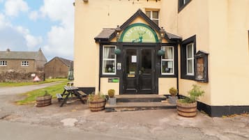 A building with a black front door, a green sign above the door, and a small garden area with potted plants.