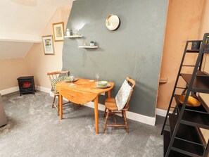 A dining area with a wooden table, chairs, a small stove, and a grey accent wall.