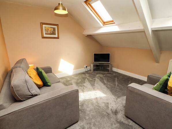 A living room with a grey sofa, a flat-screen TV, and a ceiling fan.