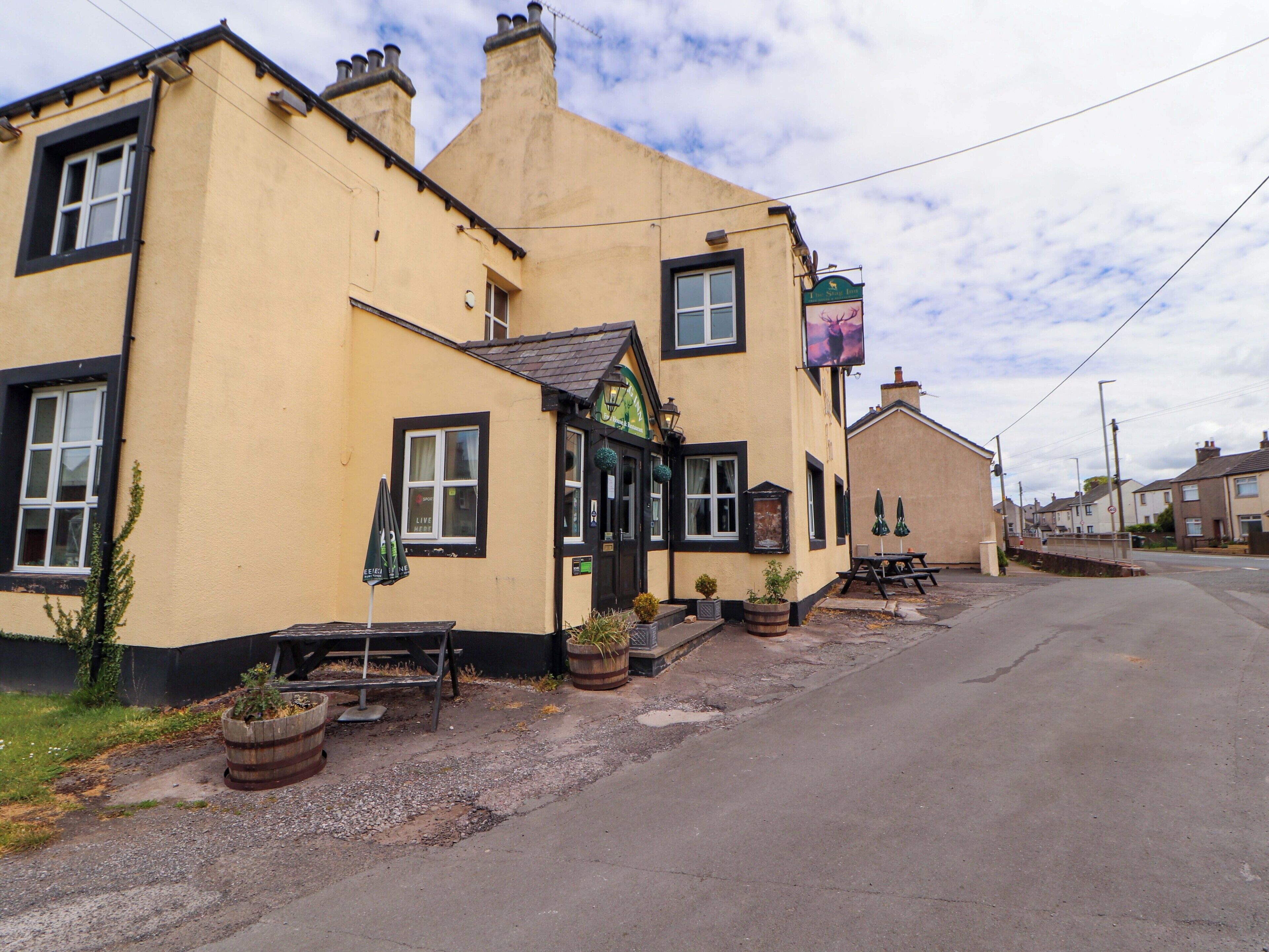 A yellow building with a pub sign, outdoor seating, and a small garden area.