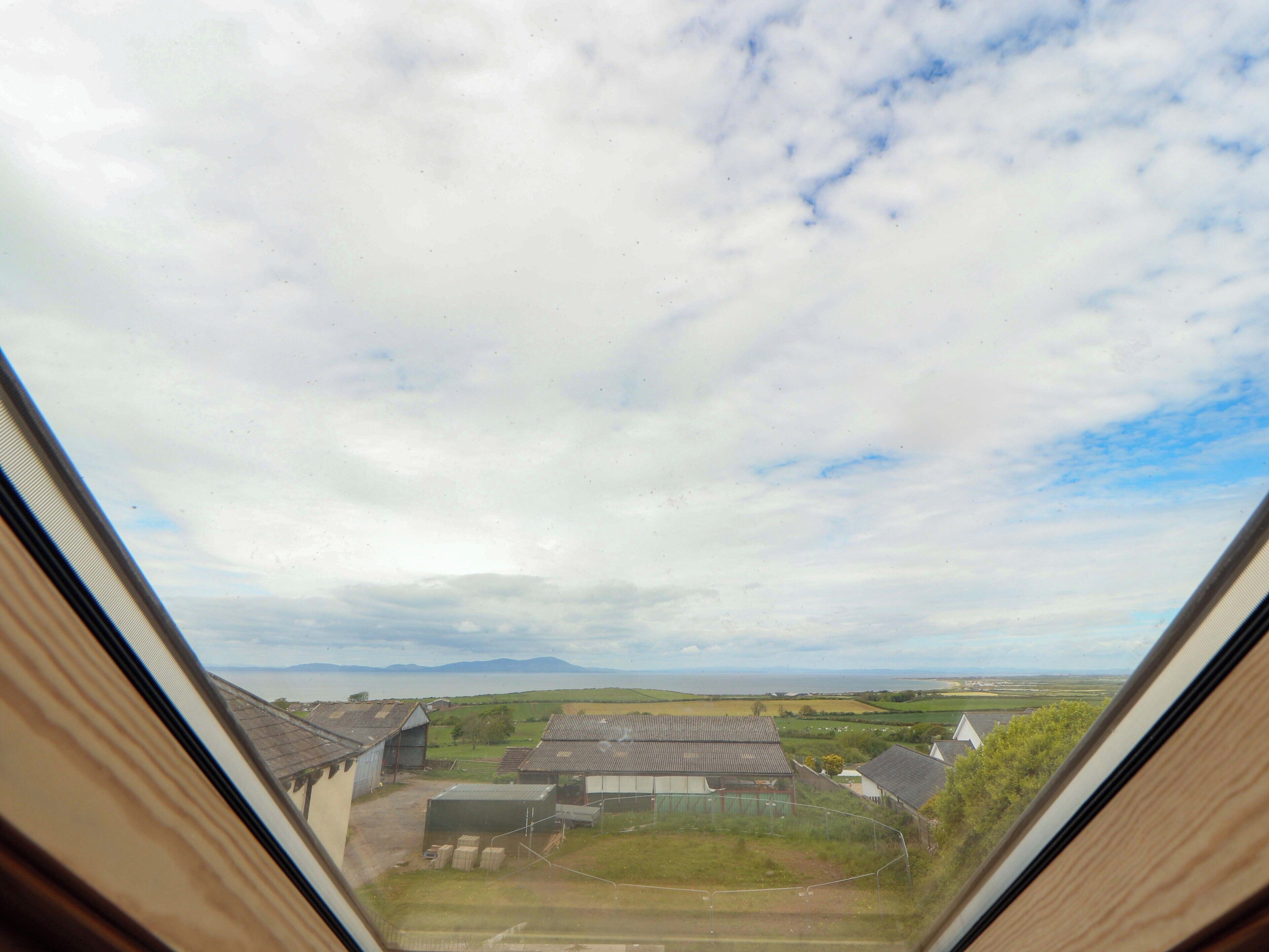 Blick durch ein Fenster auf eine ländliche Landschaft mit Häusern und offenen Feldern.