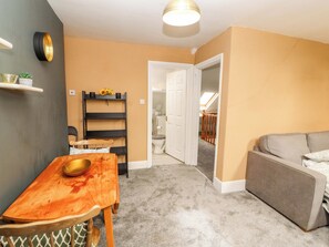 A compact living space with a dining table, a sofa, a built-in shelf, and a door leading to a bathroom. - The Loft Apartment @ The Stag Inn (Maryport)