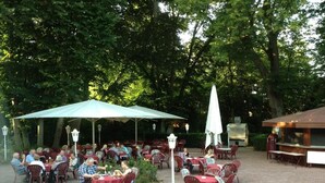 Un área de comedor al aire libre con mesas y sillas, rodeada de árboles.