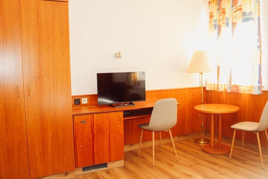 A wooden room with a TV, a desk, two chairs, and a lamp.