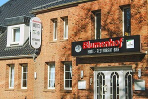 Un edificio de ladrillo con un letrero que dice 'Blumenhof HOTEL RESTAURANT BAR' y otro letrero más pequeño que dice 'Blumenhof HOTEL RESTAURANT BAR'.