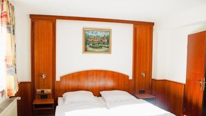 Habitación de hotel con cabecera de madera, cama con ropa blanca, un cuadro en la pared y un armario de madera.
