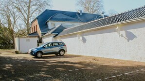 Un edificio blanco con techo azul, un coche estacionado y un camino de grava.