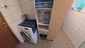 A compact laundry area with a washing machine, shelves for folded towels, and a view of the outdoors through a window.