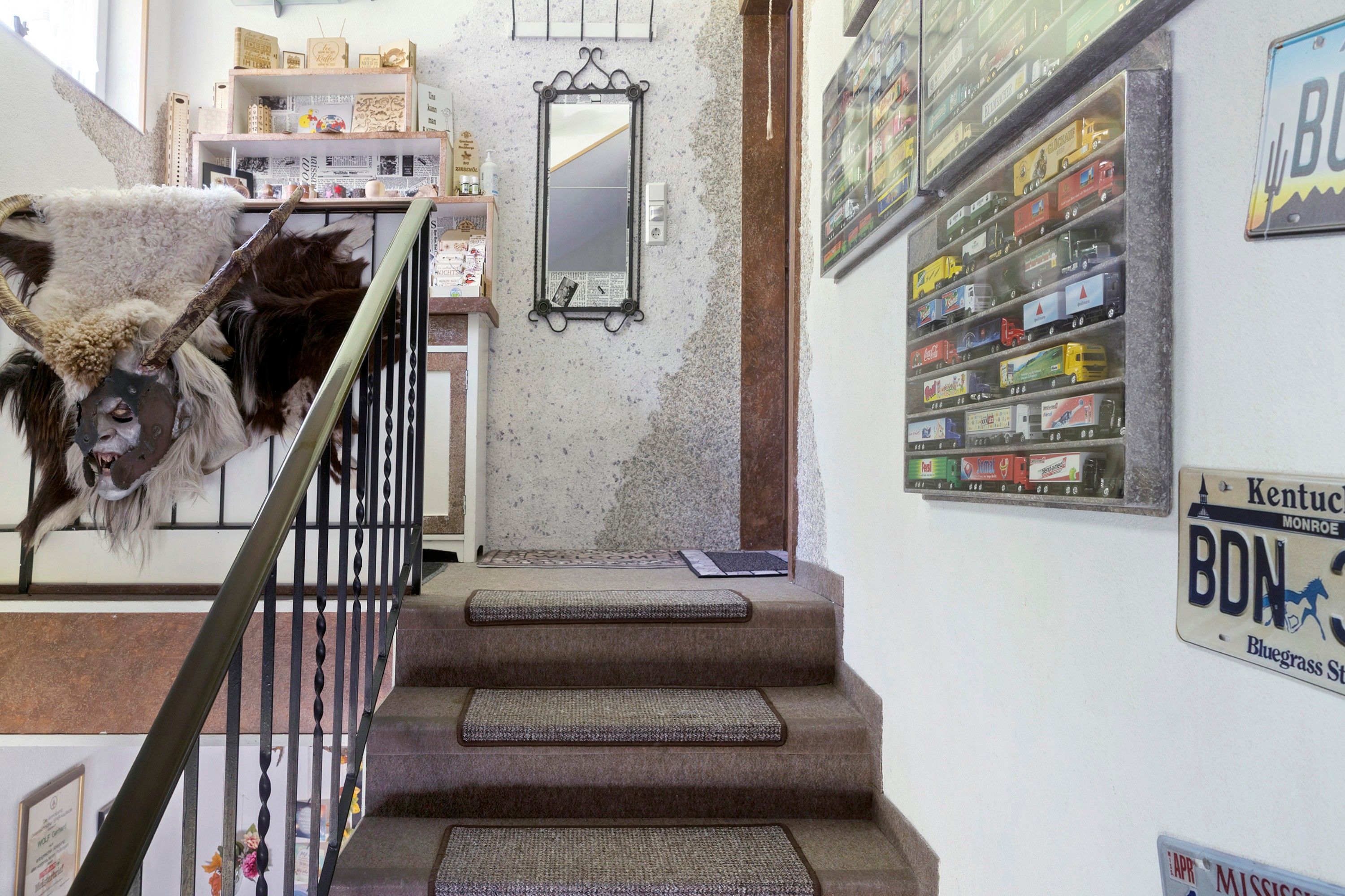 A staircase with a welcome mat, a mirror, and a wall with toy trucks.