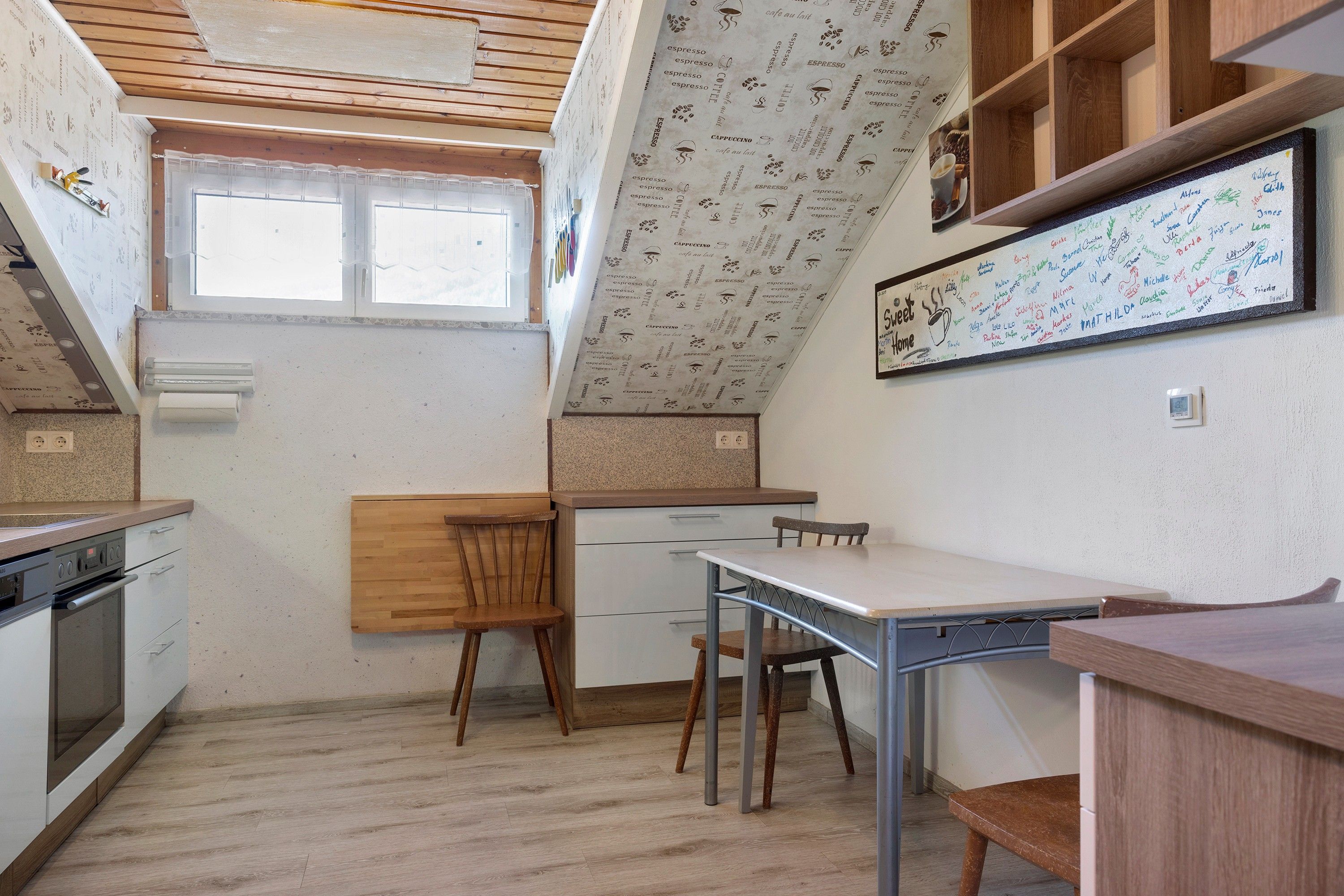 Une cuisine de taille réduite avec un plafond en bois, une fenêtre et un mur orné d’une fresque sur le thème du café.