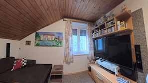 A cozy room with a TV, bookshelf, and a painting of a building.