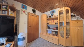 A room with a television, a white heater, wooden cabinets with glass doors, and a clock on the wall.