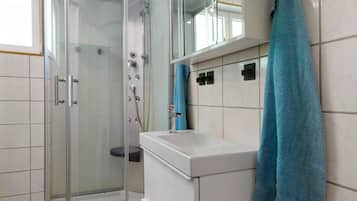 Un baño moderno con ducha de vidrio, un lavamanos blanco y una toalla azul.