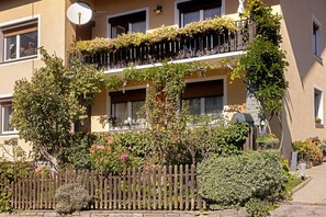 Een meerlaags gebouw met balkons vol bloeiende planten, een stenen muur en een houten hek.