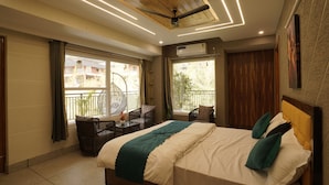 Un dormitorio con cama, ventilador de techo, ventana, balcón y zona de estar con mesa y sillas.